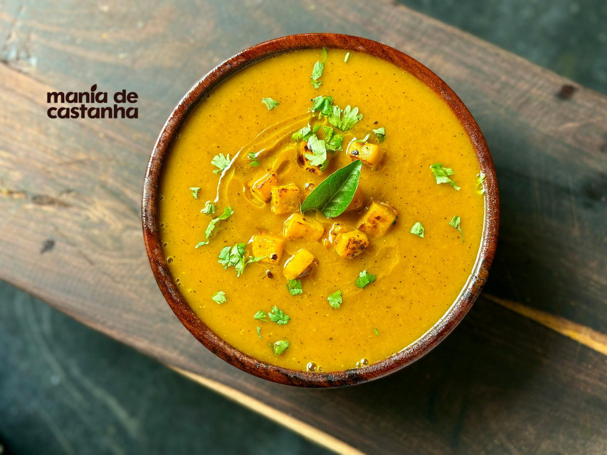 Sopa cremosa low carb com cubos dourados e ervas frescas servida em tigela de barro sobre tábua rústica – Mania de Castanha